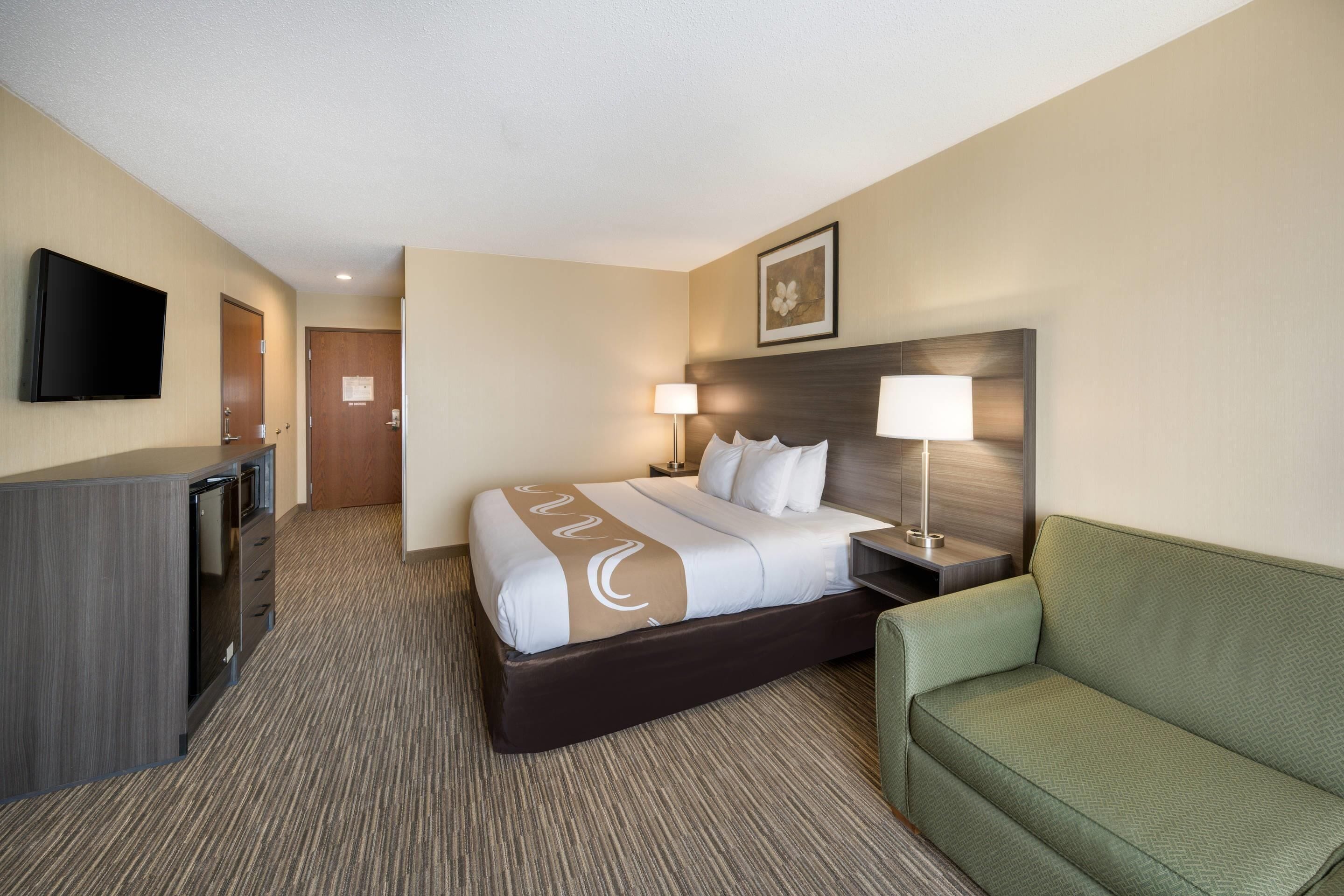 A hotel room with a bed, bedside lamps, a television, a desk, and a green sofa.