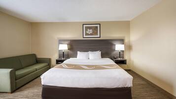 A hotel room with a large bed, a green sofa, two bedside tables with lamps, and a framed picture on the wall.