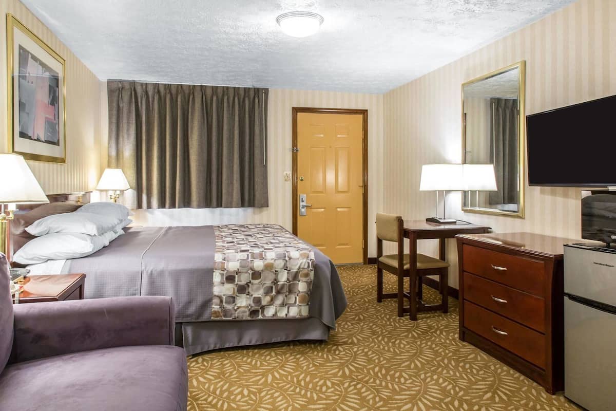 A hotel room with a bed, a desk, a chair, a dresser, a television, and a door.