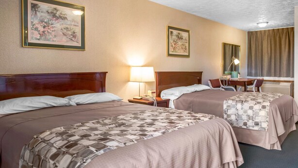 A hotel room with two beds, a desk, a chair, a lamp, and two framed pictures on the wall. - Rodeway Inn & Suites Branford - Guilford (Branford)