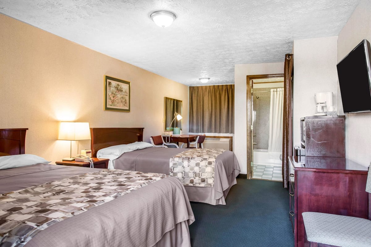 A hotel room with two beds, a desk, a chair, a TV, and a coffee maker.