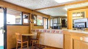 A compact kitchen with wooden cabinets, a small dining area with two chairs, a refrigerator, and a television. - Rodeway Inn & Suites Branford - Guilford (Branford)