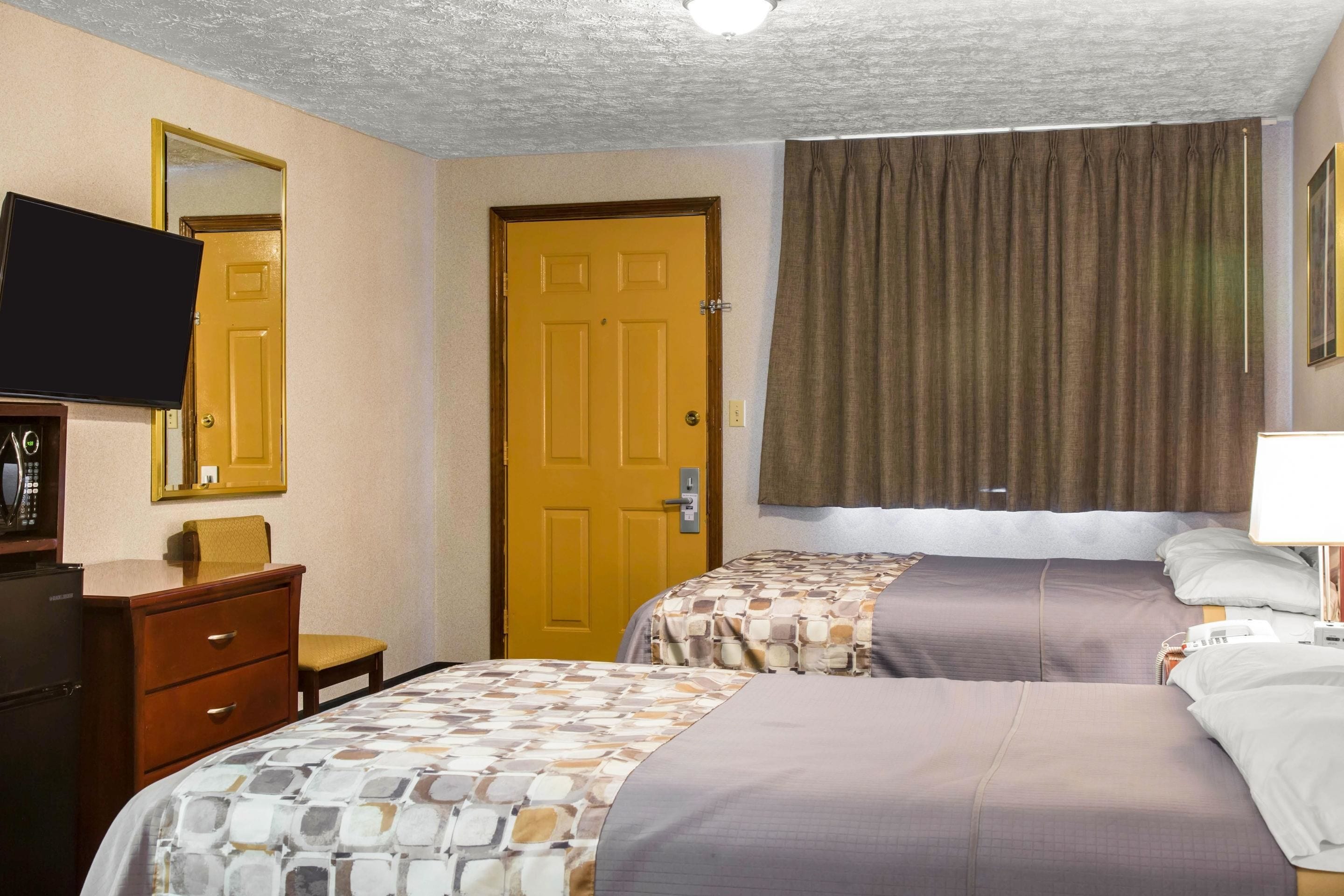 Una camera d'albergo con due letti, una televisione, un comò e una porta.