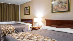 A hotel room with two beds, a nightstand with a lamp, and two framed pictures on the wall. - Rodeway Inn & Suites Branford - Guilford (Branford)