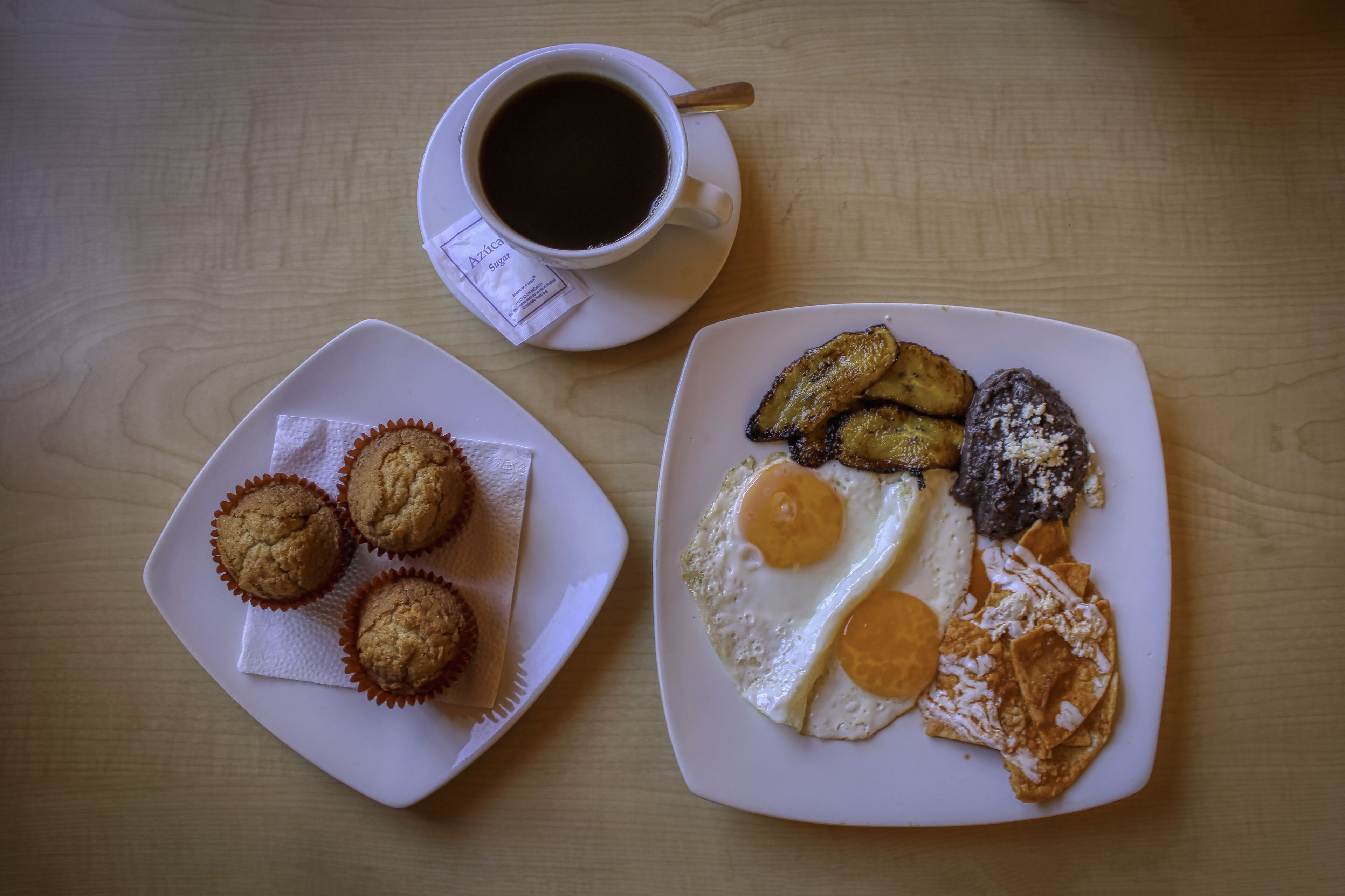 Un plato de desayuno con muffins, huevos fritos y plátanos fritos sobre una mesa de madera.