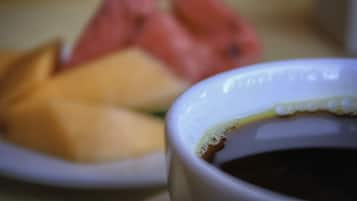 A close-up of a white ceramic cup with a beverage, possibly coffee, and a blurred background featuring a plate with food items.