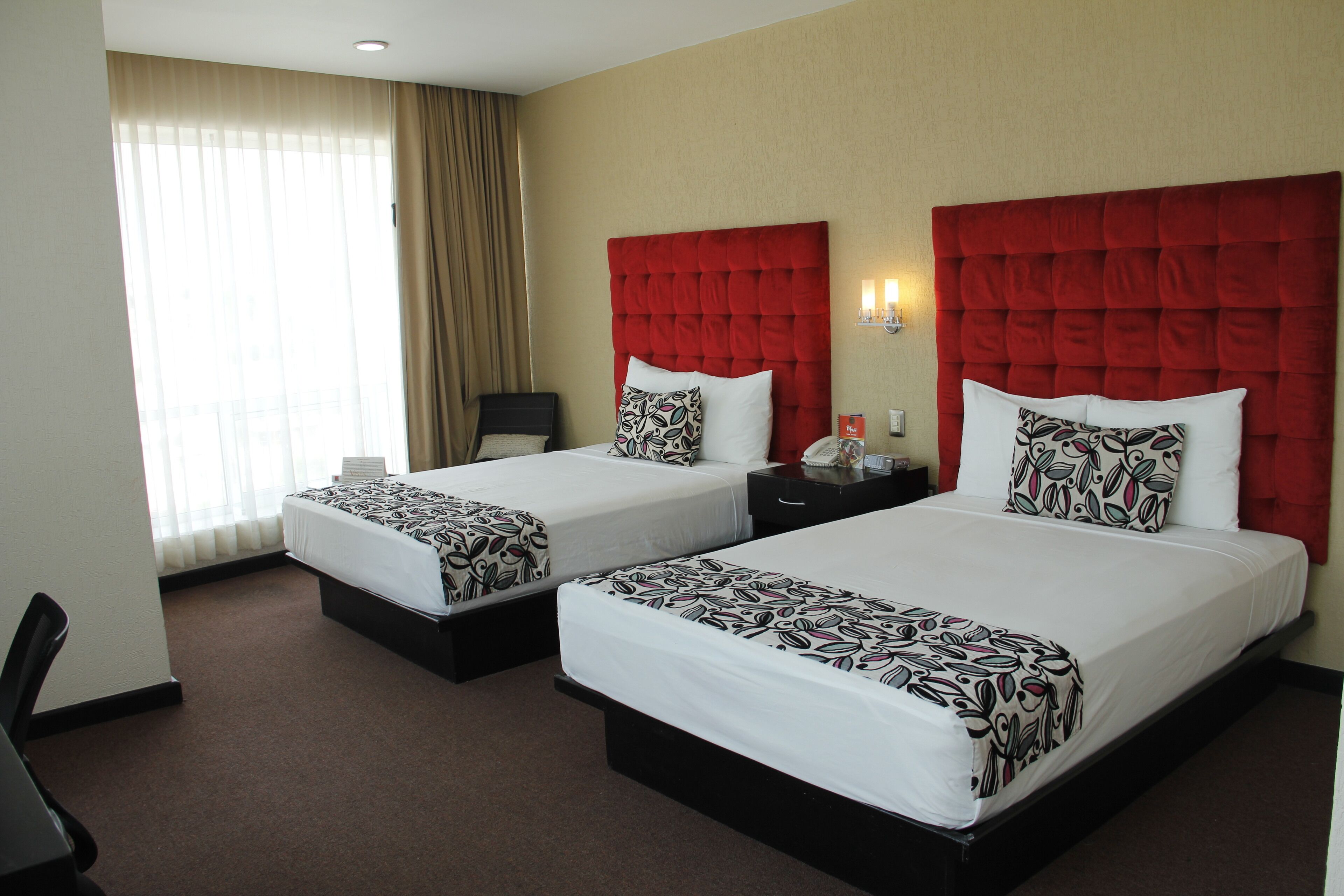 Een hotelkamer met twee bedden, elk met een rode hoofdbord, een bureau en een stoel.