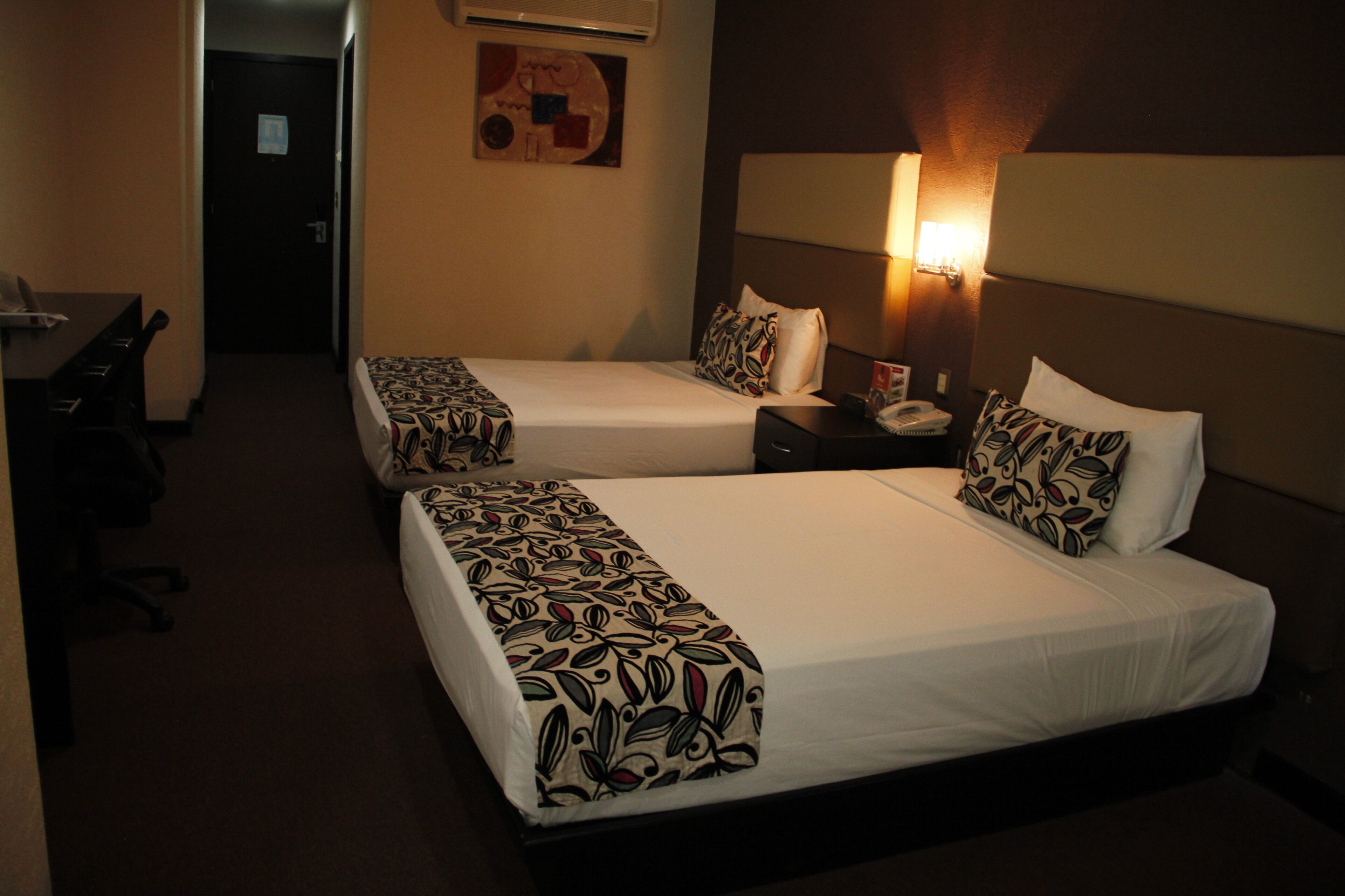 A hotel room with two beds, a desk, and a chair.