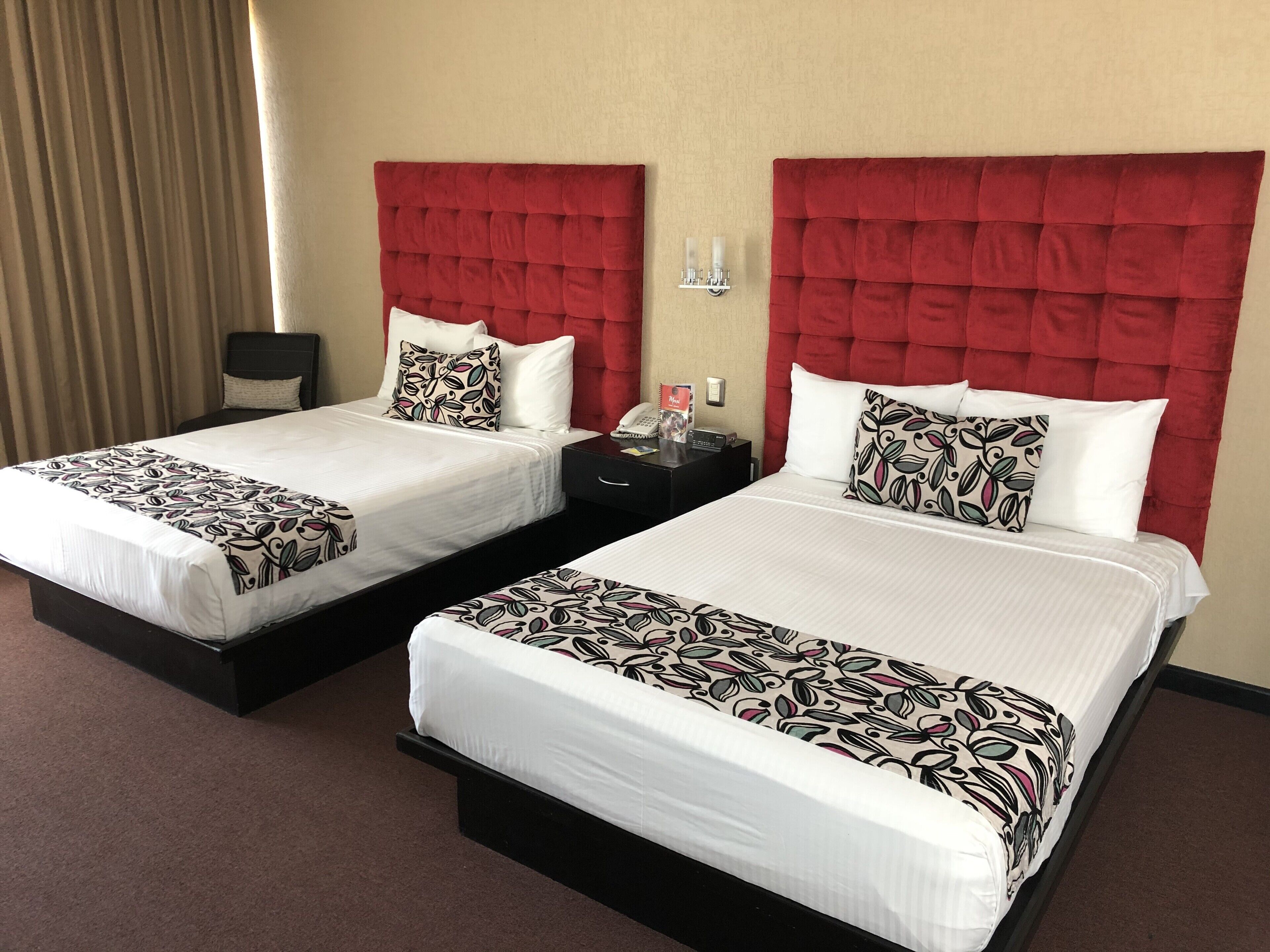 Dos camas dobles con cabeceros rojos, ropa de cama blanca y almohadones estampados.