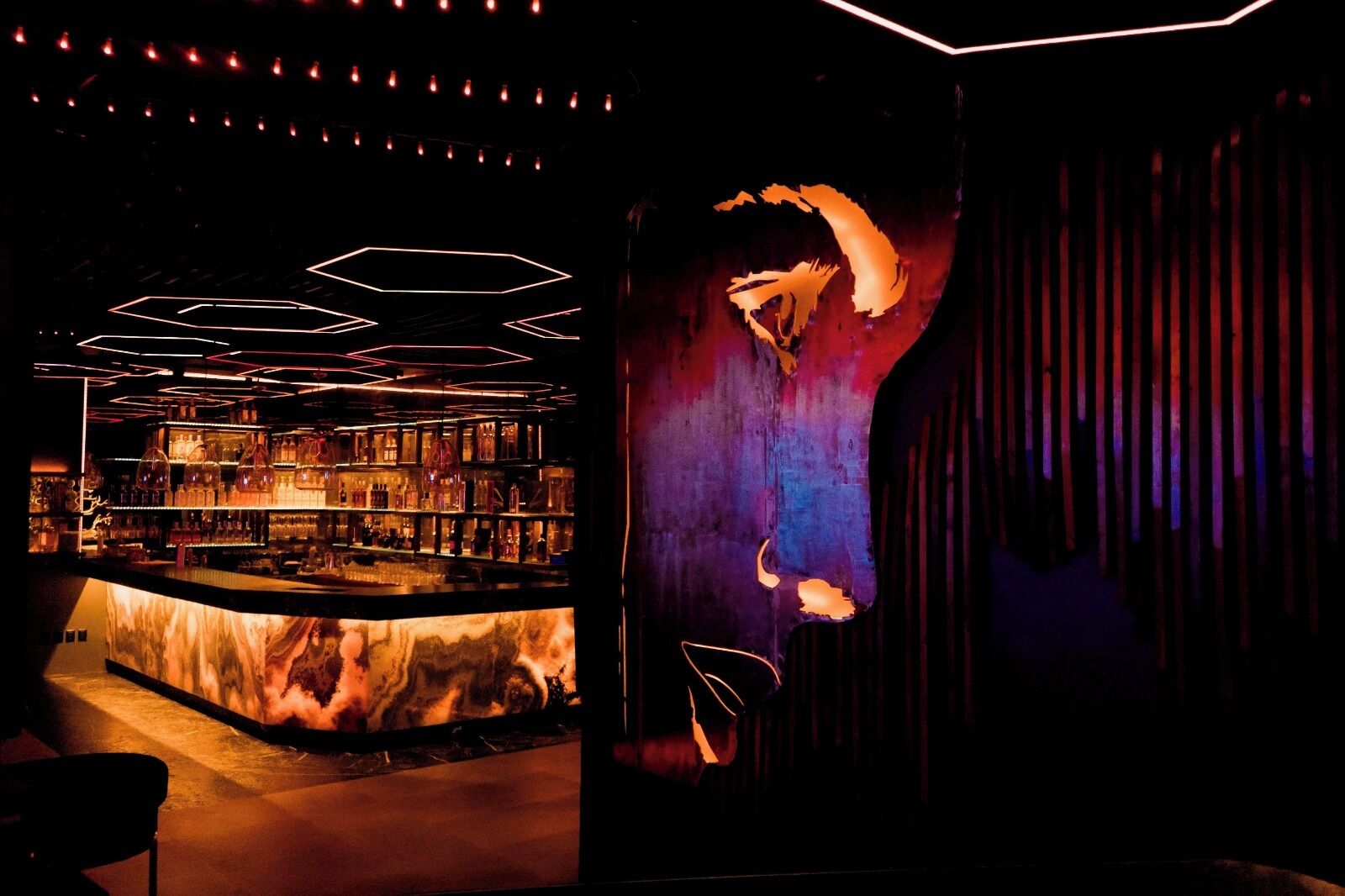 A bar area with a marble countertop and overhead geometric lighting.