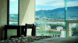 Una habitación con un ventanal grande que da a una vista urbana, destacando una cruz en una colina.