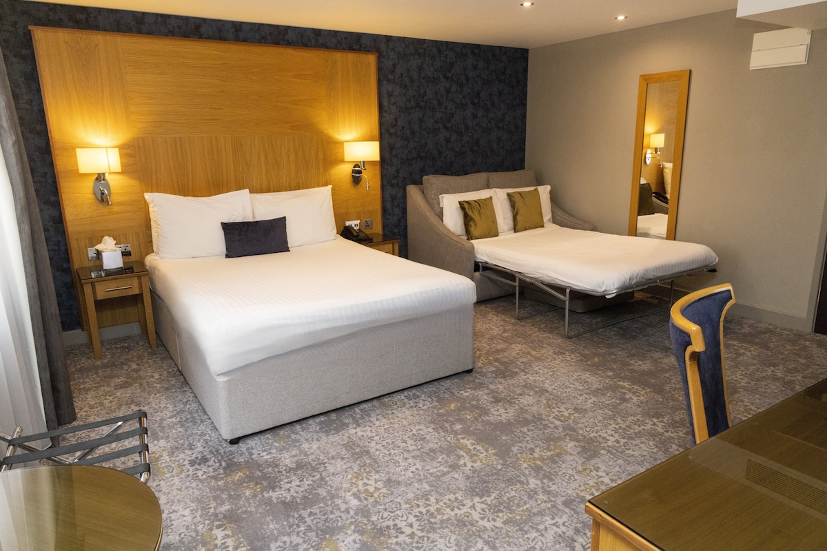 A hotel room with a large bed, a smaller bed, a desk, and a chair.