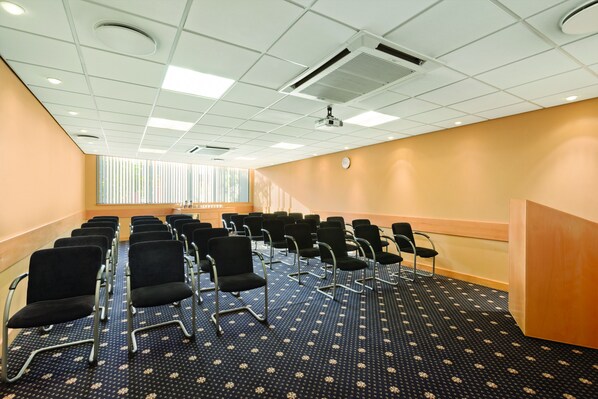 A conference room with rows of black chairs, a wooden reception desk, and a patterned carpet.