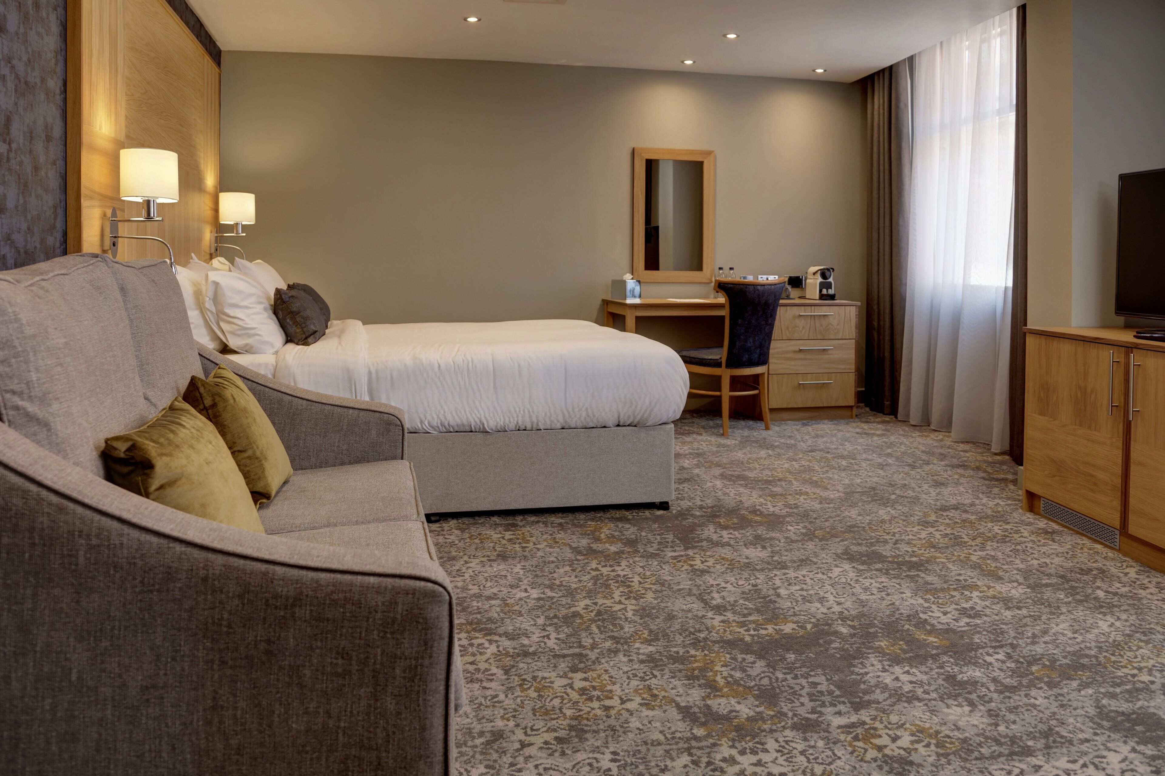 A hotel room with a bed, a sofa, a desk, a chair, a television, and a wardrobe.