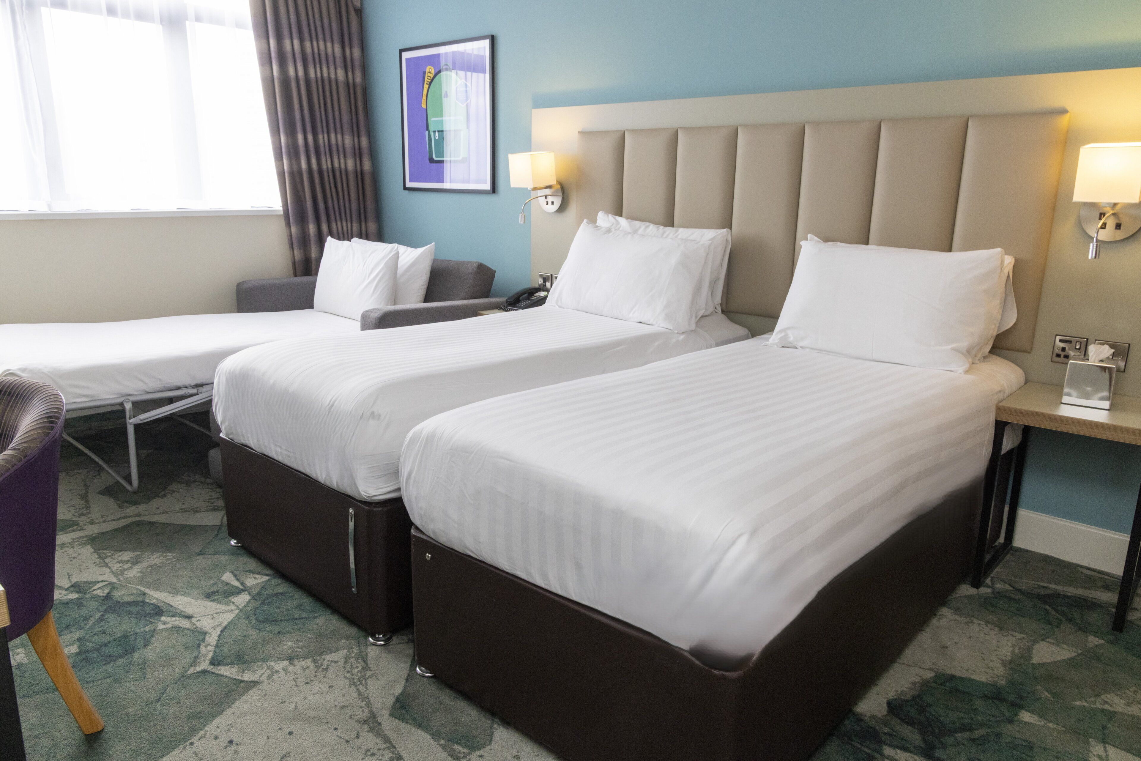 A hotel room with two beds, a desk, a chair, and a window with curtains.