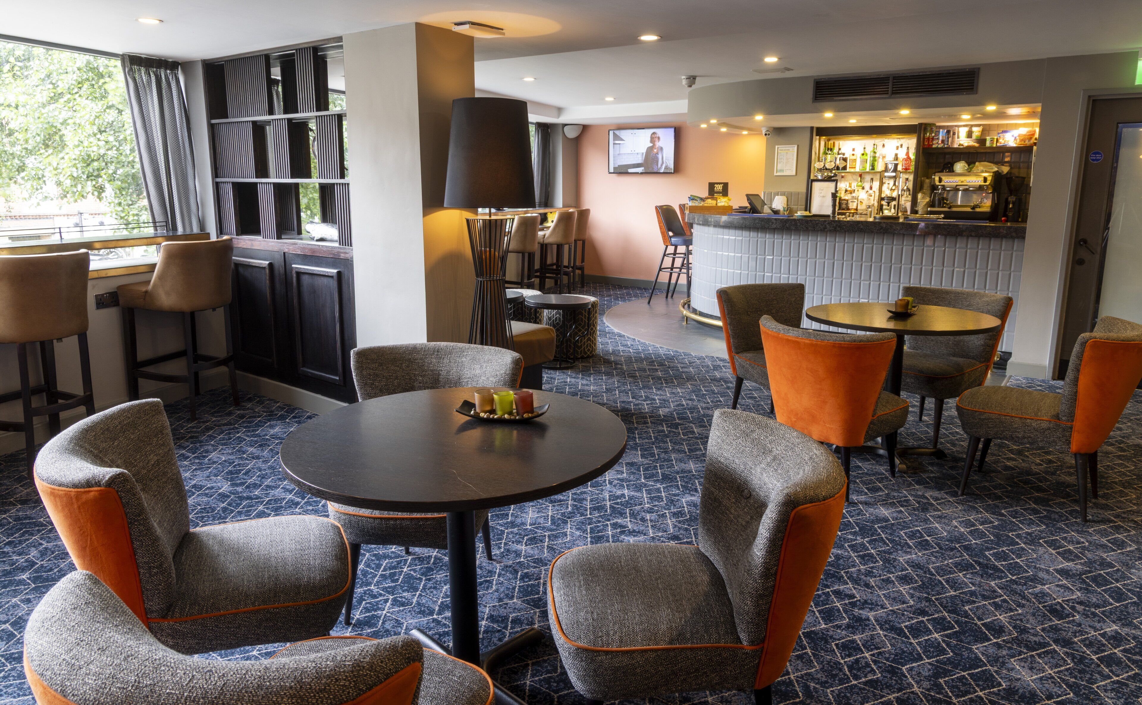 A hotel lobby with round tables, bar area, and seating.