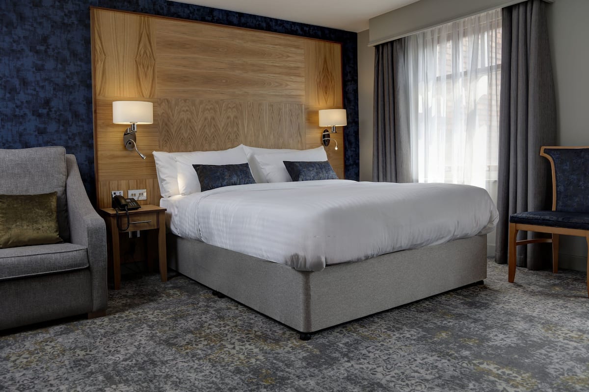 Une chambre d’hôtel avec un grand lit, deux lampes de chevet, une table de chevet, une chaise et une fenêtre avec des rideaux.