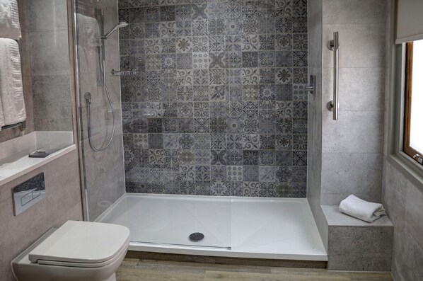 A shower area with a glass door, a white toilet, and a patterned tile wall.