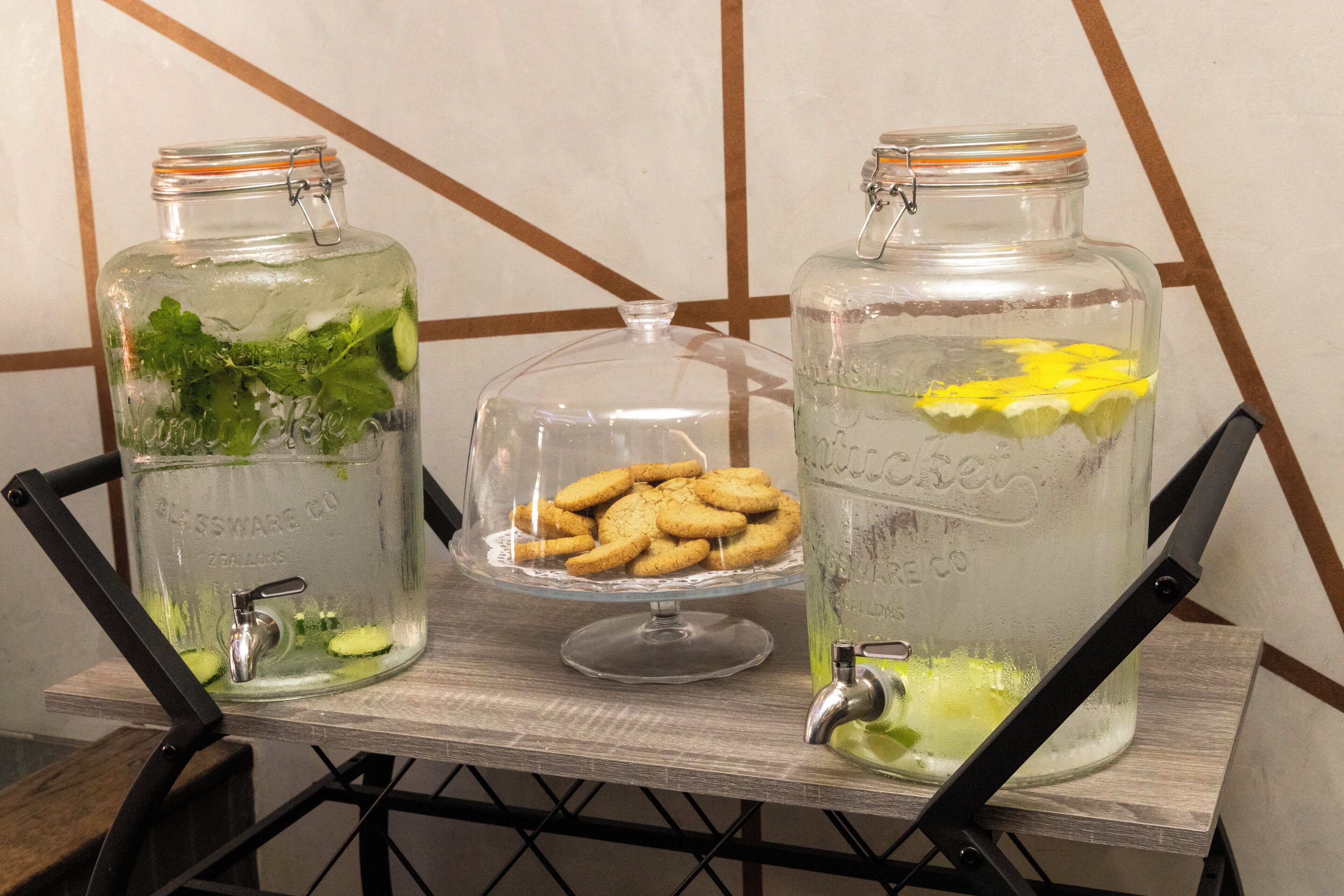Two glass jars with water and mint leaves, one with cookies on a glass stand, and a metal chair in the foreground.