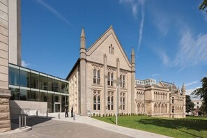 A historic building with a large glass entrance, a well-maintained lawn, and a clear blue sky.