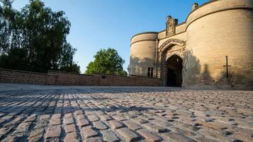 A cobblestone courtyard with a brick wall and a stone building with a large arched entrance.