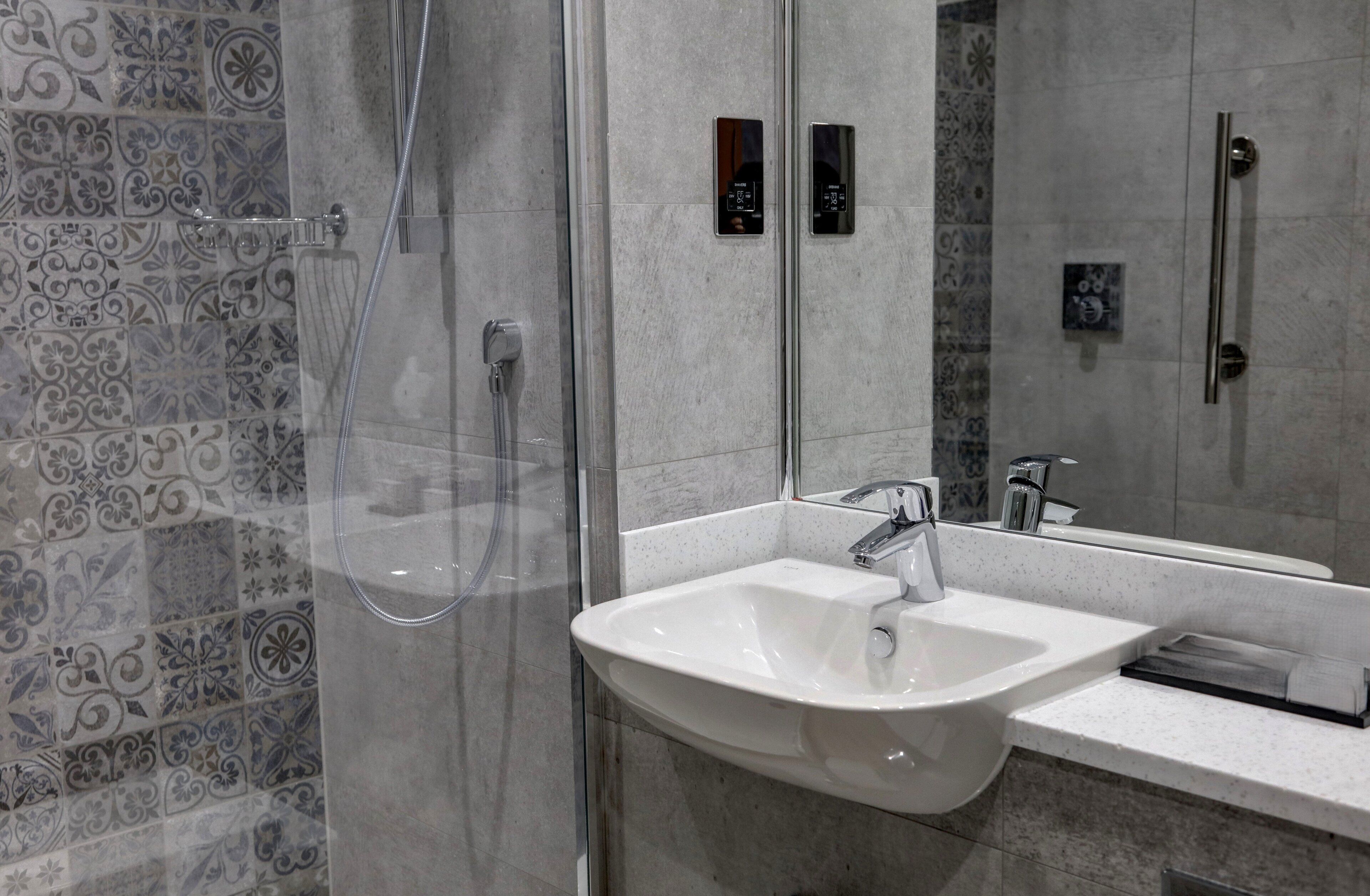A modern bathroom with a glass-enclosed shower, a white sink, and a large mirror.