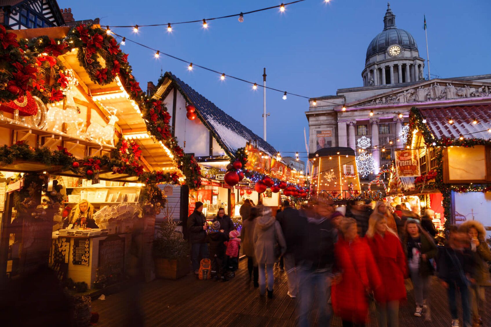 A bustling market street at dusk with festive decorations and a prominent building with a dome in the background.