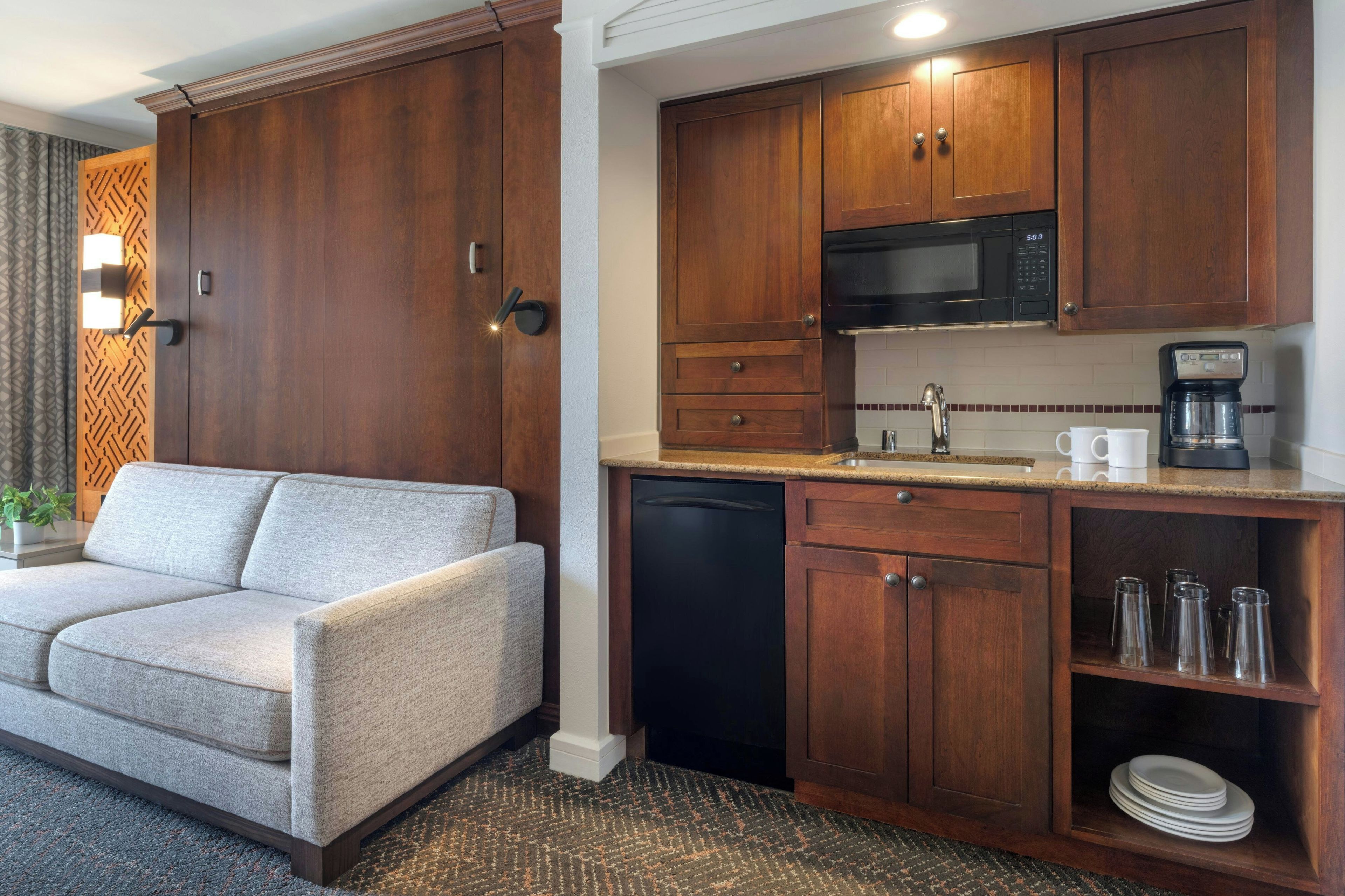 Habitación de hotel compacta con sofá, kitchenette y un pequeño comedor.