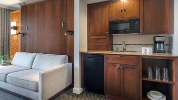 Habitación de hotel compacta con sofá, kitchenette y un pequeño comedor.