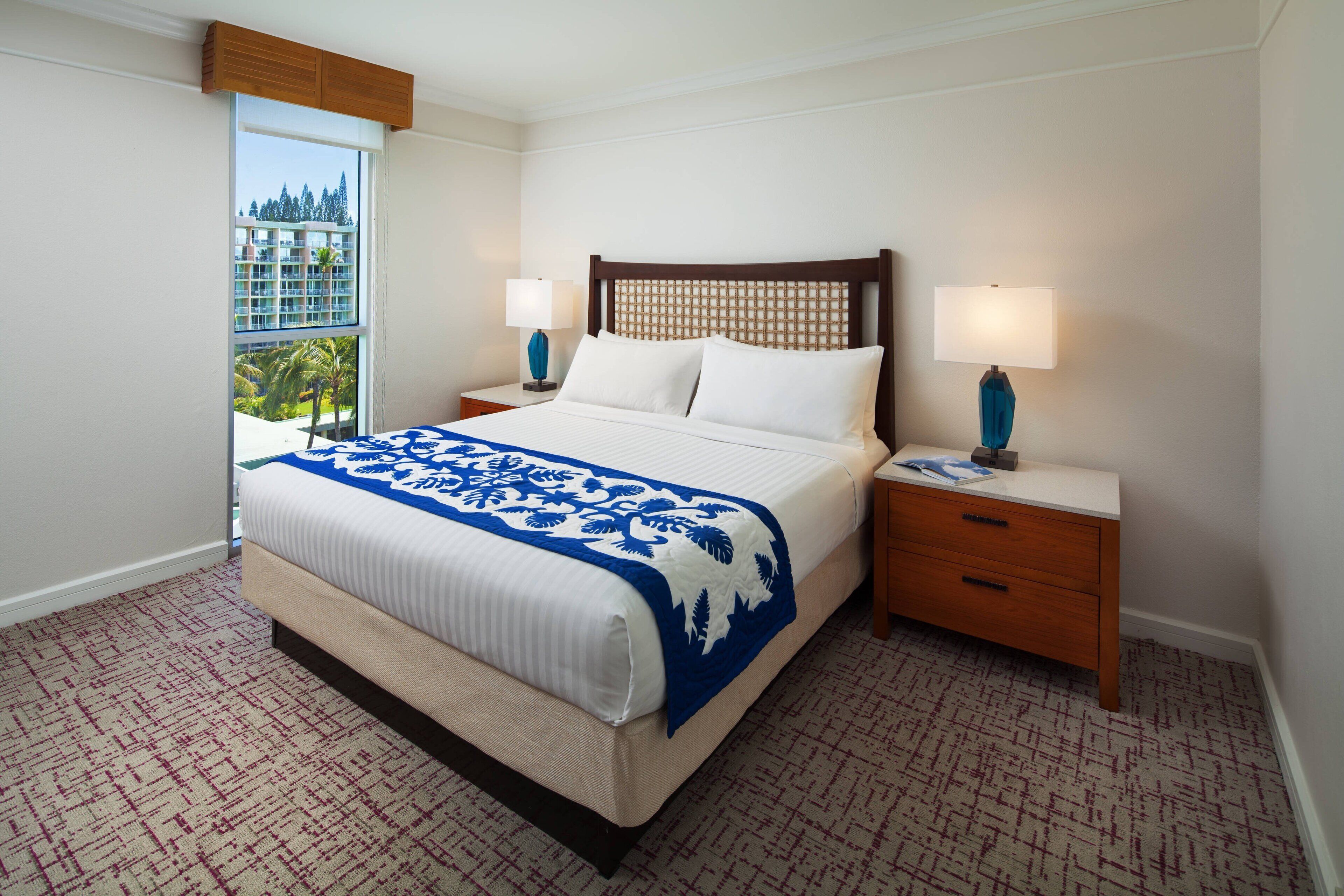 A hotel room with a large bed, two bedside tables, and a view of a building through a window.