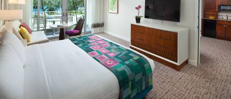 A hotel room with a large bed, a TV, a dining area with a table and chairs, and a view of the outdoors.