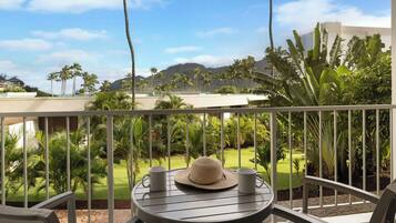 Un balcón con mesa, sillas y vistas a un paisaje tropical con palmeras y montañas.