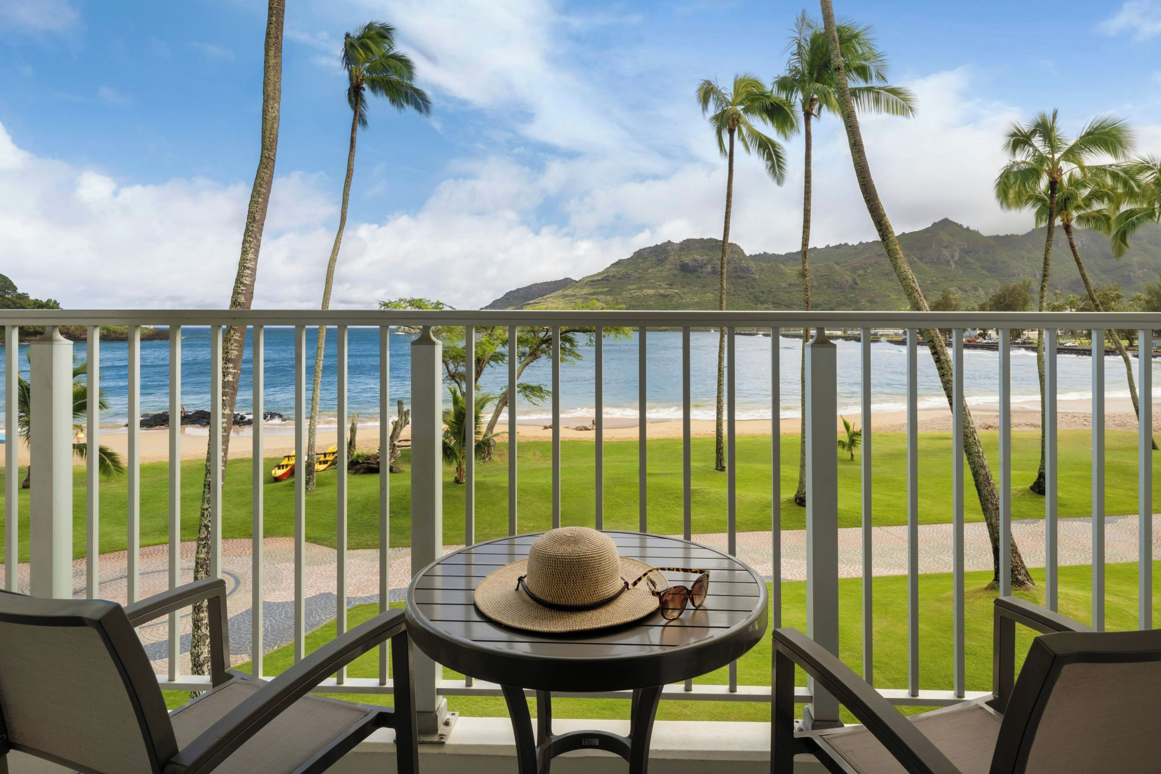 A balcony with a view of a beach, palm trees, and a mountain in the distance.