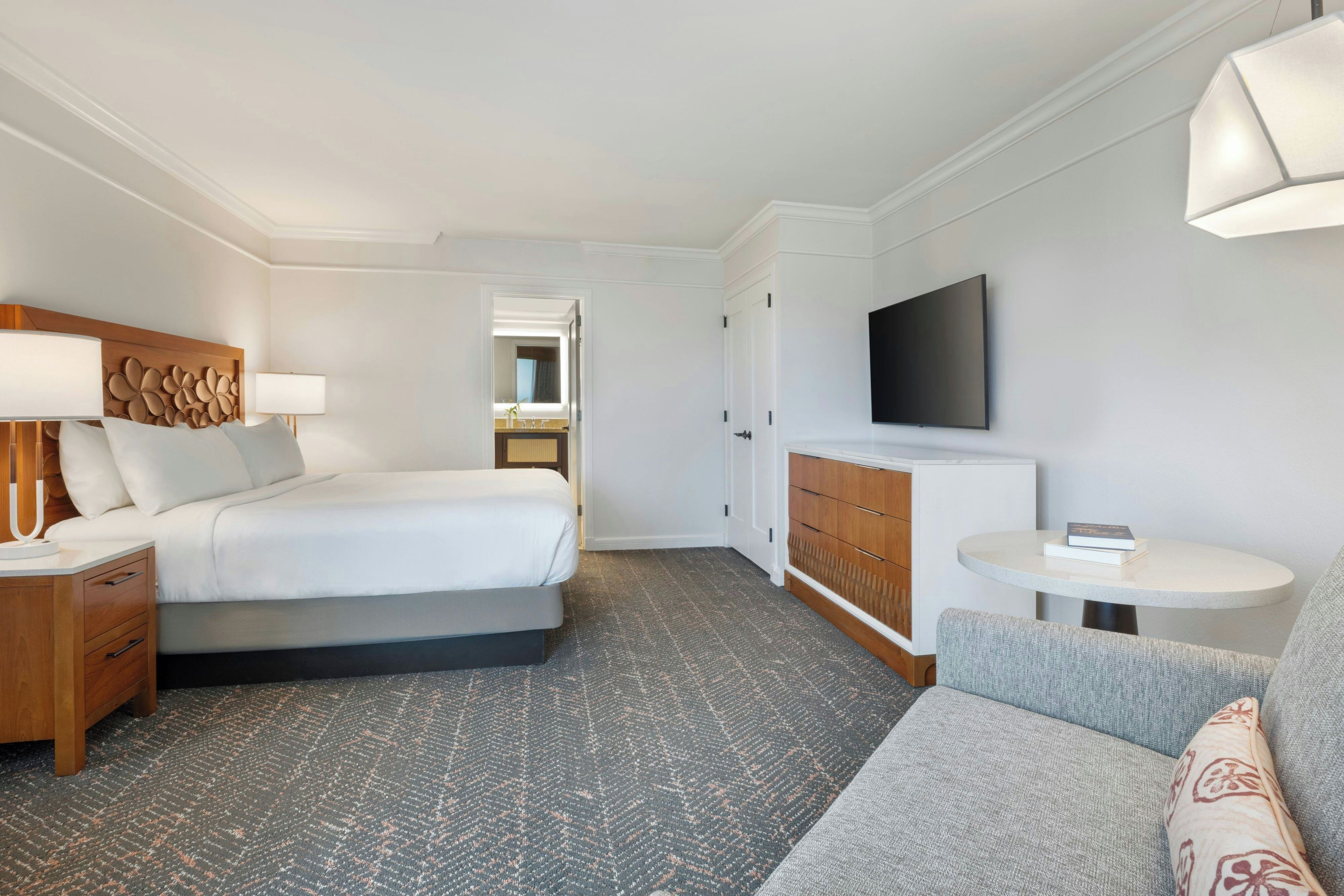 Ein Hotelzimmer mit einem Bett, Nachttisch, Lampe, Kommode, Fernseher und einem kleinen runden Tisch mit einem Buch.