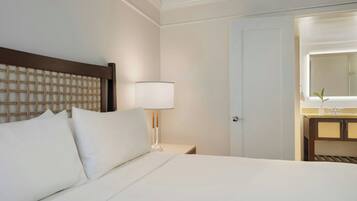 Habitación de hotel con cama, mesita de noche, lámpara, espejo y baño visible a través de una puerta abierta.