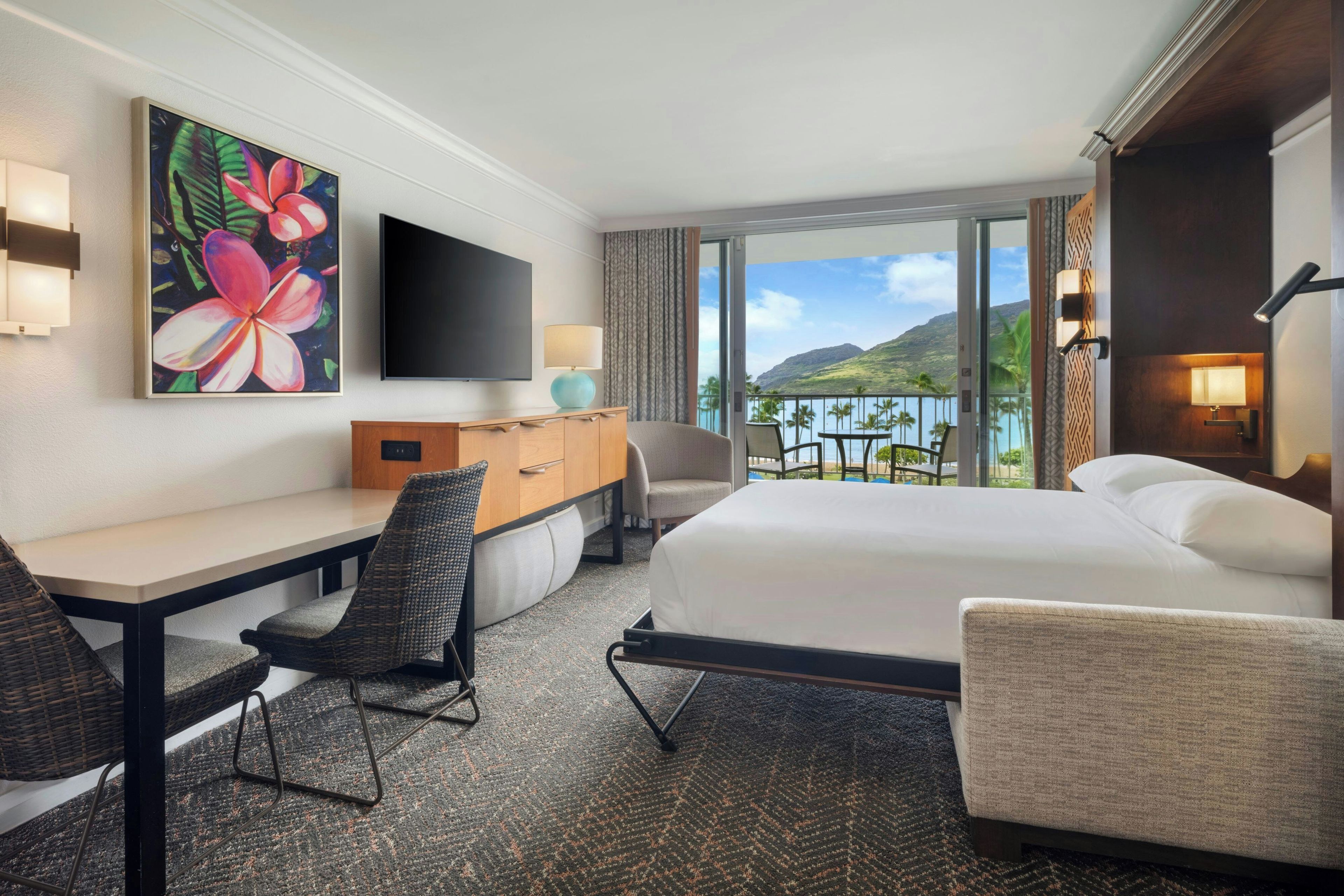A hotel room with a bed, a desk, a chair, a television, and a view of the mountains.
