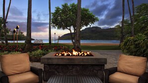 A fire pit with two wicker chairs, a stone table, and a view of the beach and ocean.