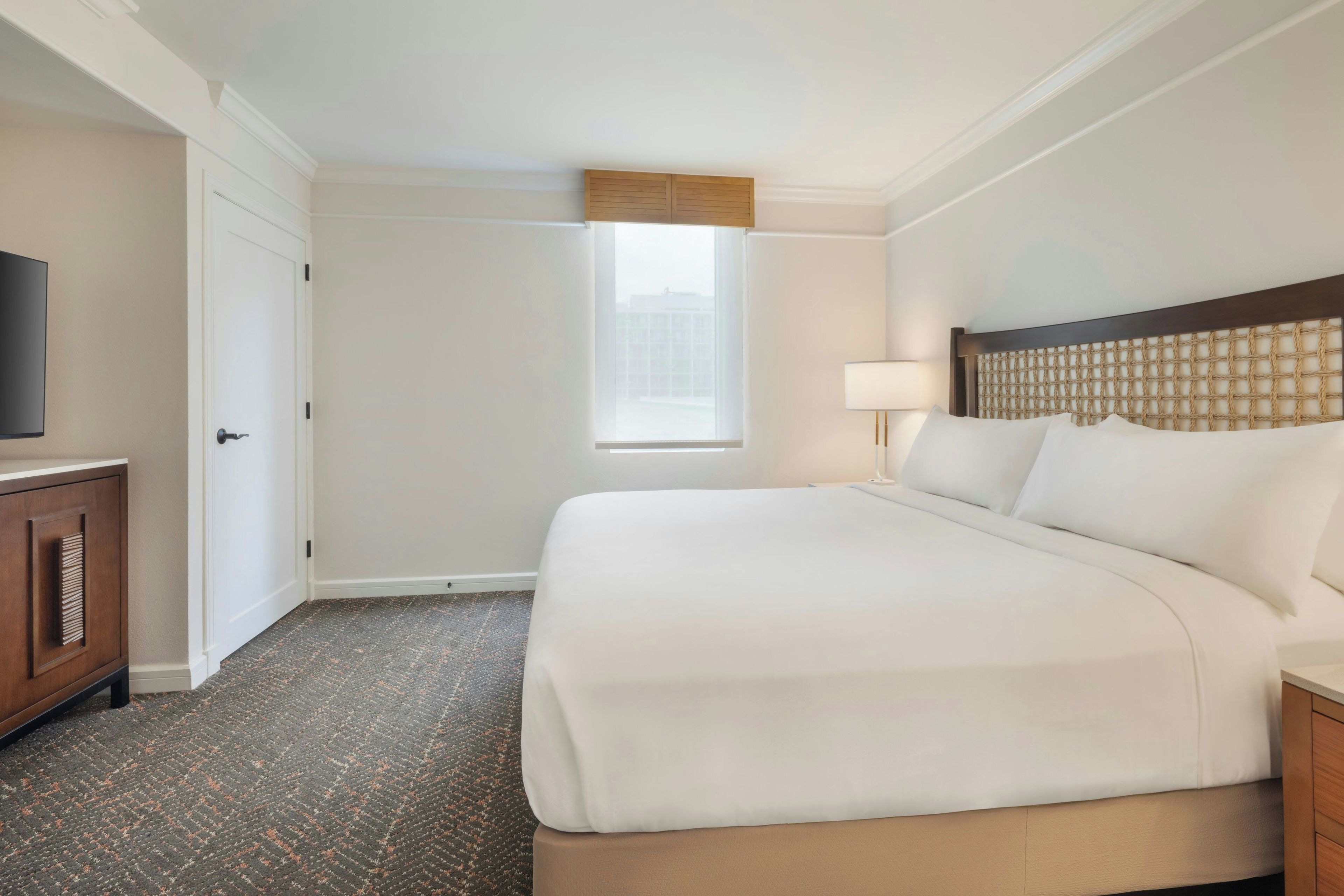 Een hotelkamer met een groot bed, een televisie op een kast, een raam met uitzicht en een deur.