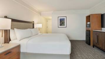 Una habitación de hotel con cama, mesitas de noche, escritorio, televisor y armario.