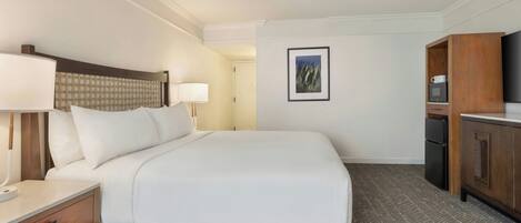 Quarto de hotel com cama, mesas de cabeceira, escrivaninha, televisão e guarda-roupa.