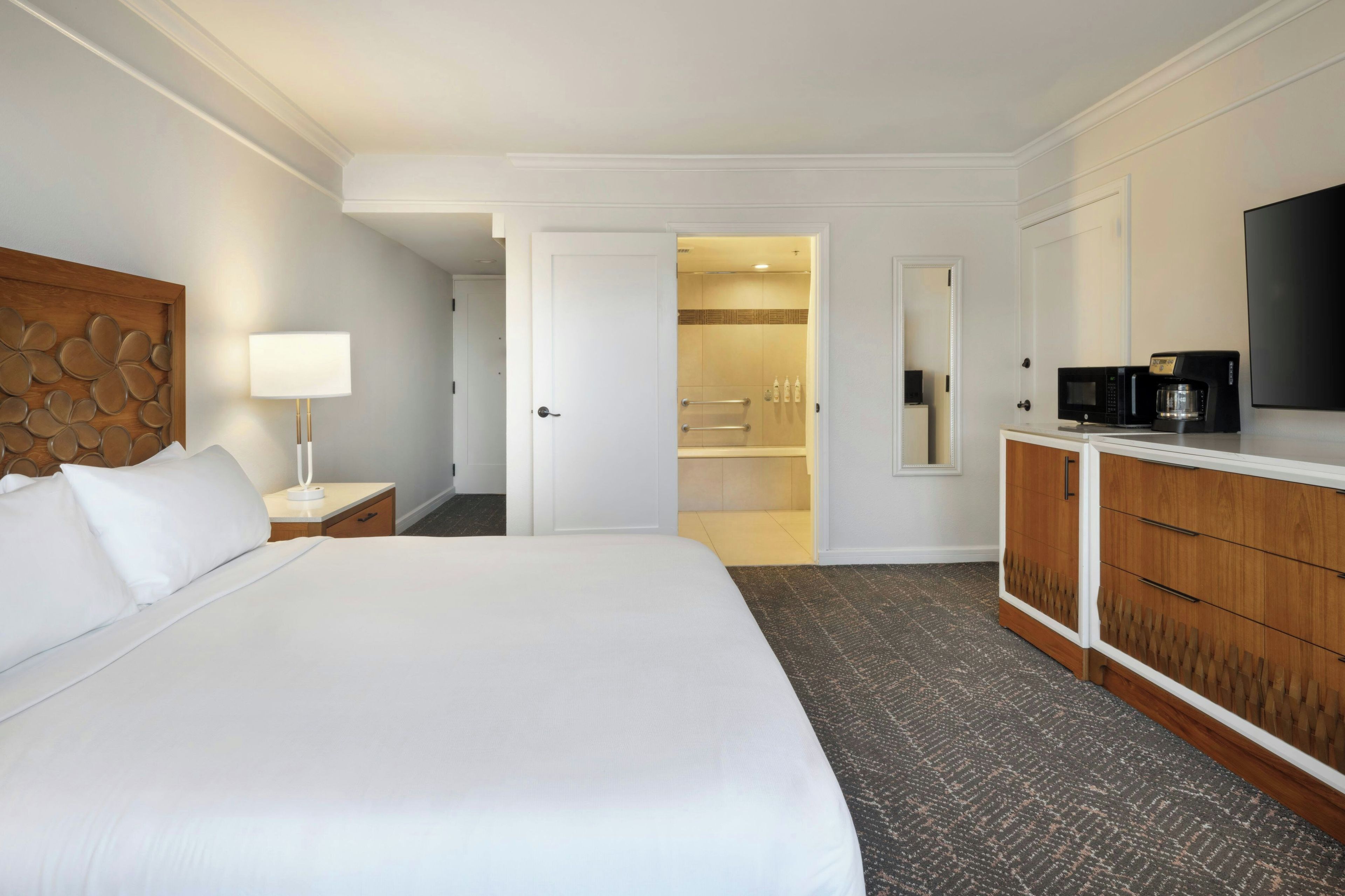 A hotel room with a large bed, a bedside lamp, a wardrobe, a television, and a bathroom visible through an open door.