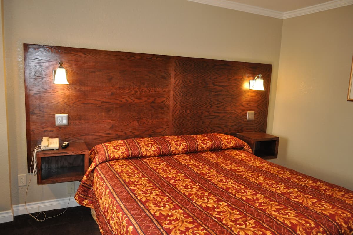 A hotel room with a wooden headboard, a bed with a red and gold patterned bedspread, bedside lamps, and a telephone on a nightstand.
