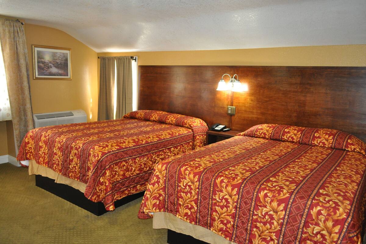A hotel room with two beds, a nightstand with a lamp, a framed picture on the wall, and a window with curtains.