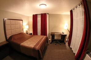 A hotel room with a bed, desk, chair, and two lamps.