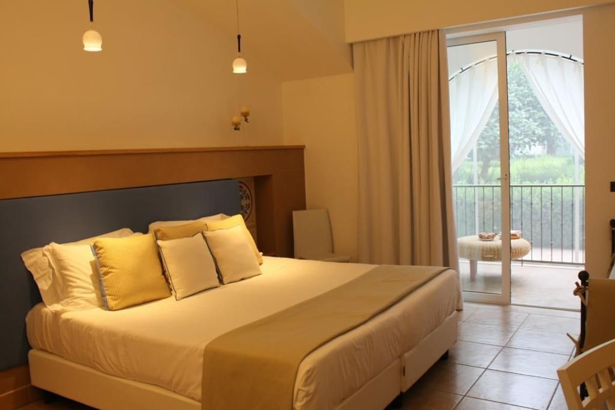 A bedroom with a large bed, a chair, a table, and a balcony with curtains.
