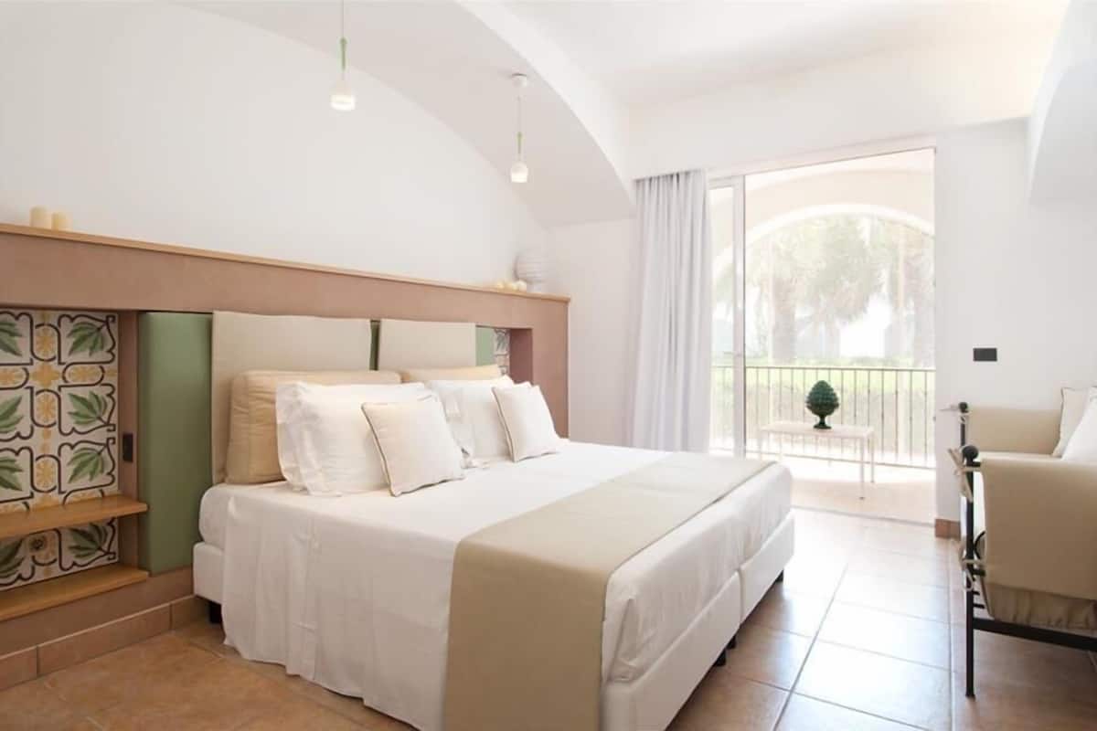 A bedroom with a bed, a chair, a balcony with a view, and a decorative headboard.