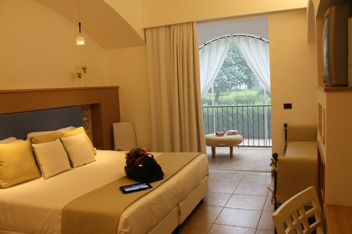 A hotel room with a bed, a chair, a small table, and a balcony with a view.