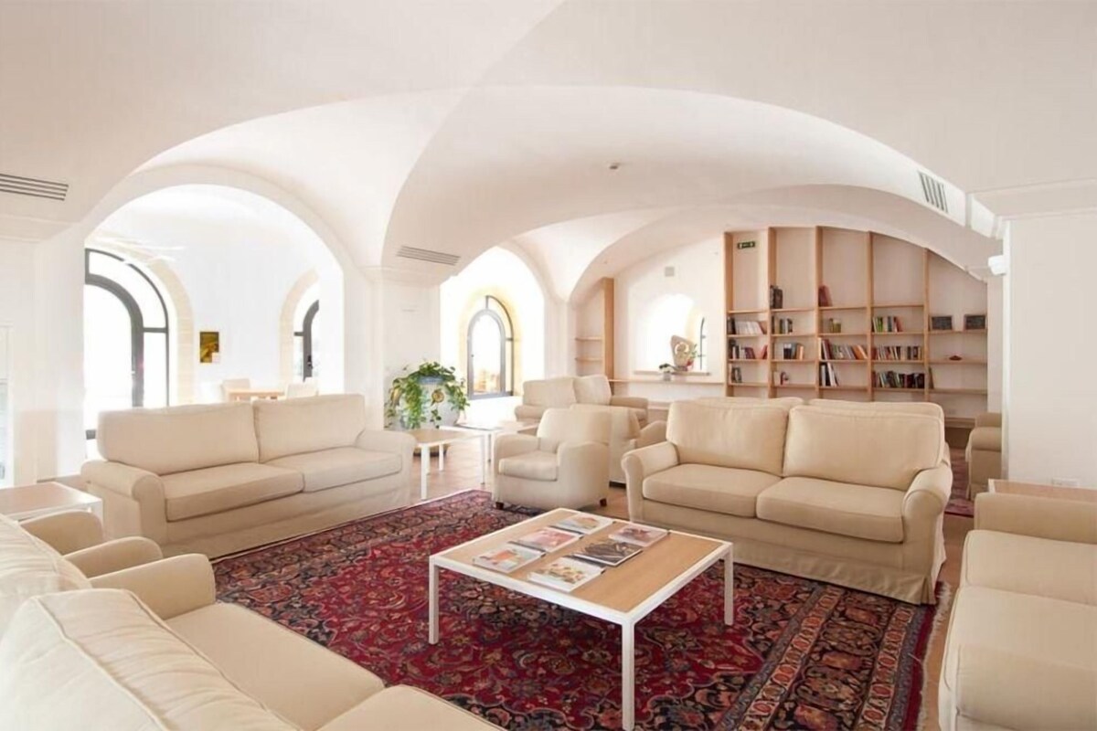 A spacious living room with high ceilings, arched windows, and a central coffee table.