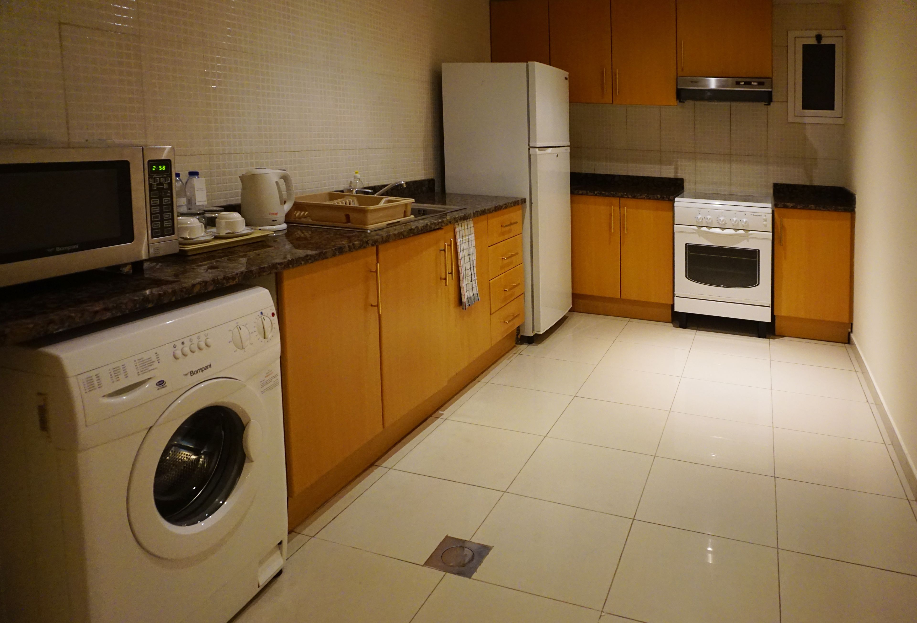 A compact kitchen with a washing machine, microwave, refrigerator, oven, and wooden cabinets.