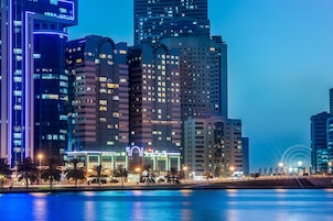 Un paisaje urbano con modernos rascacielos, un paseo marítimo y un paseo iluminado.